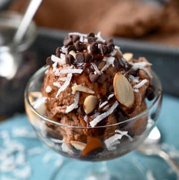 close up of a parfait dish of vegan ice cream topped with coconut, almonds, chocolate chips and chocolate drizzle