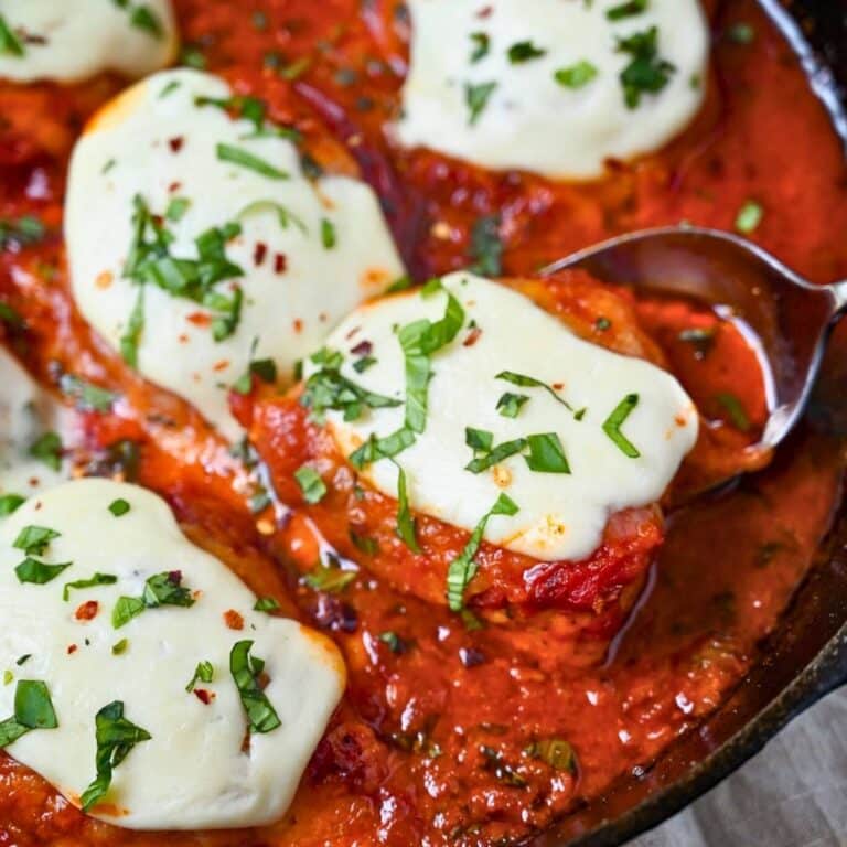 a skillet with chicken breasts topped with marinara, pepperoni, and mozzarella with fresh basil on top