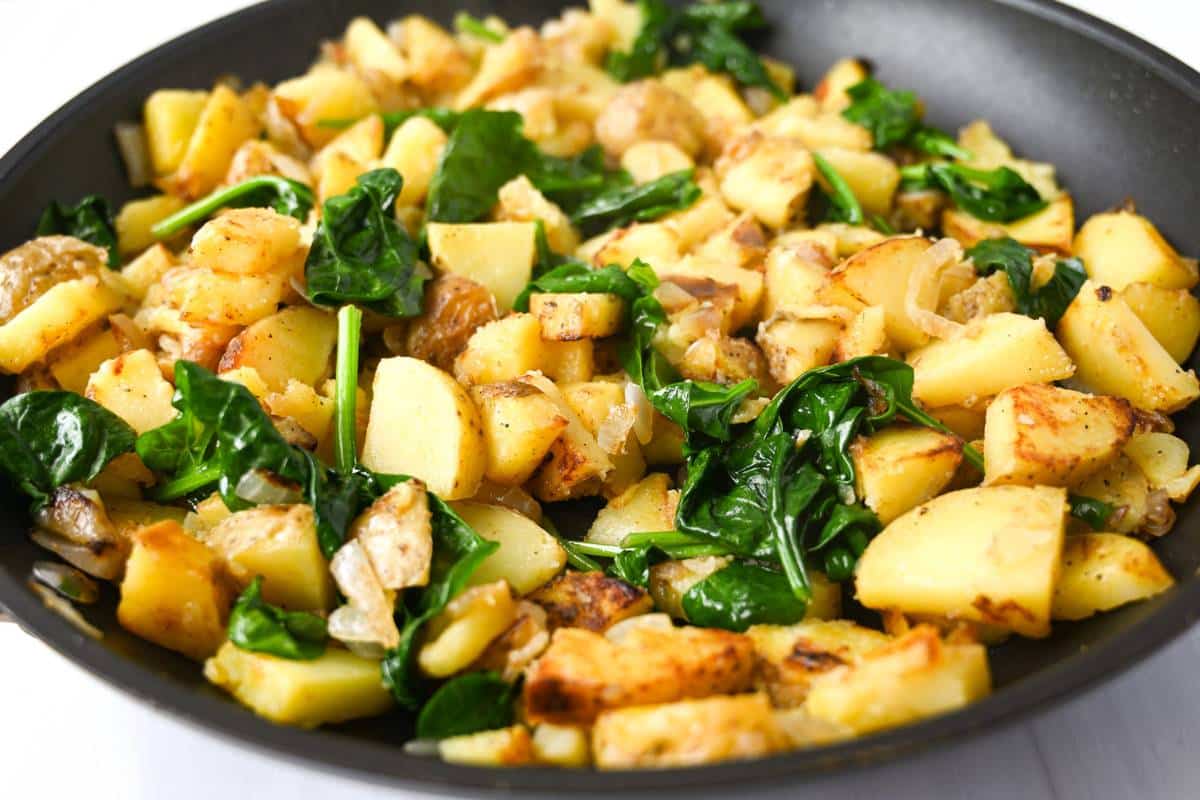 spinach wilted in with cooked potatoes in a skillet