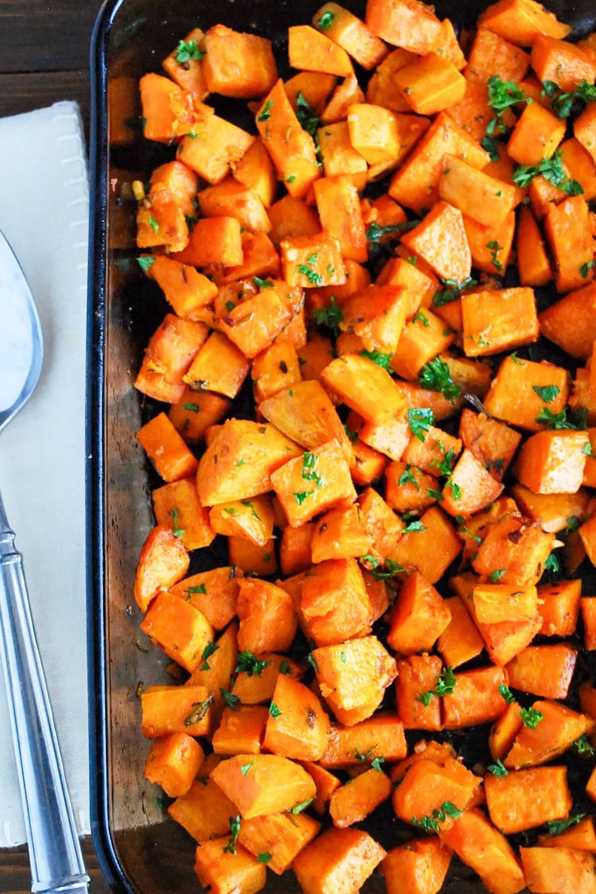 looking down at a pan of roasted sweet potatoes with a serving spoon and napkin