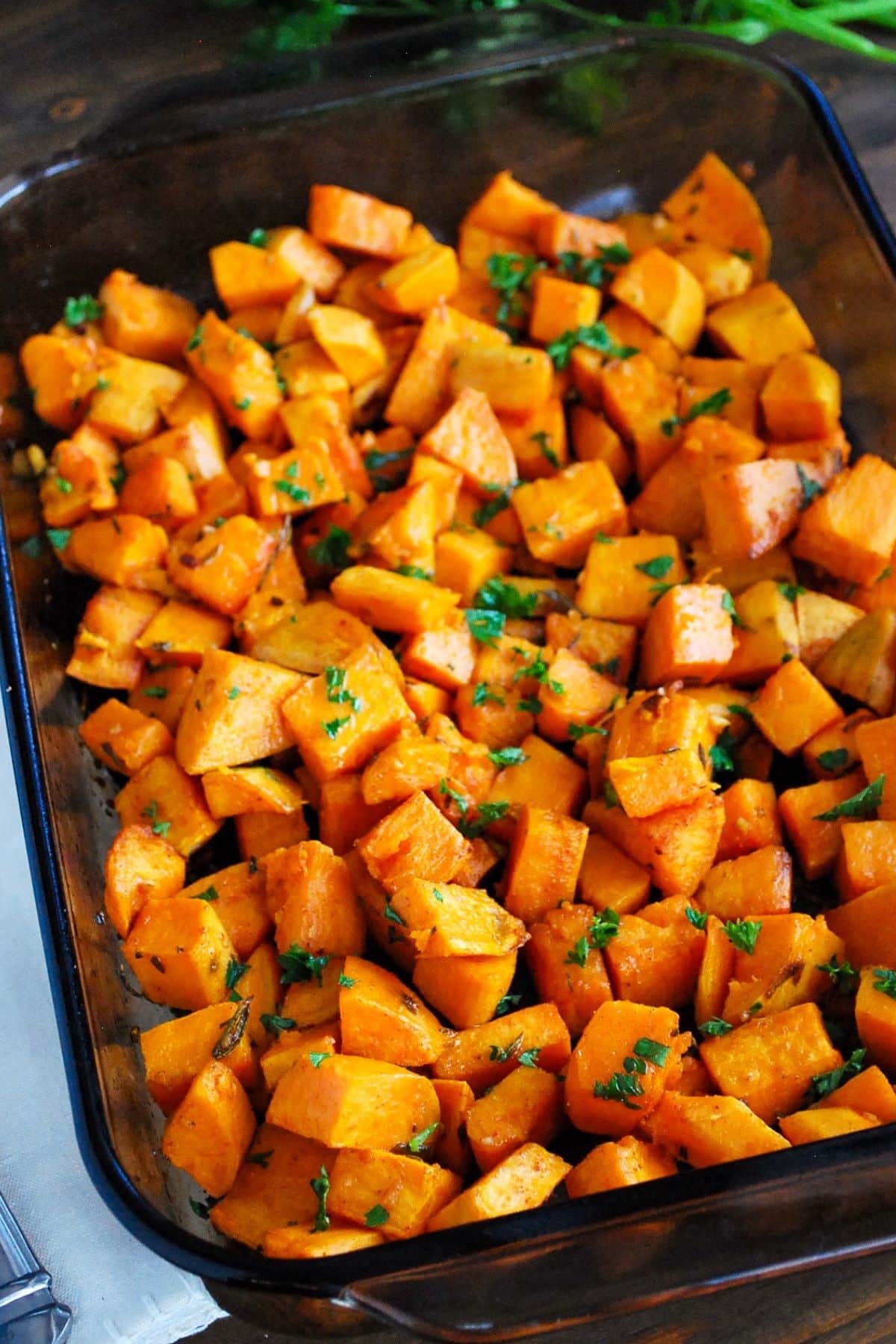 roasted sweet potatoes with rosemary, parsley, and garlic in a baking dish