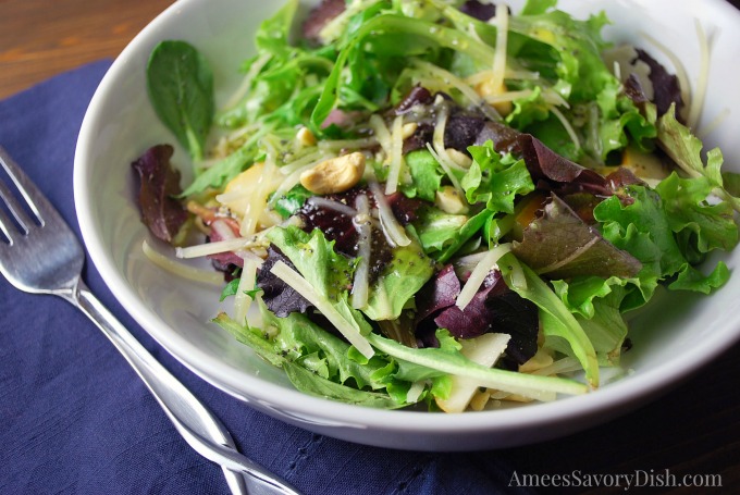 Close up of a mixed green salad with nuts, cheese, and dressing on top