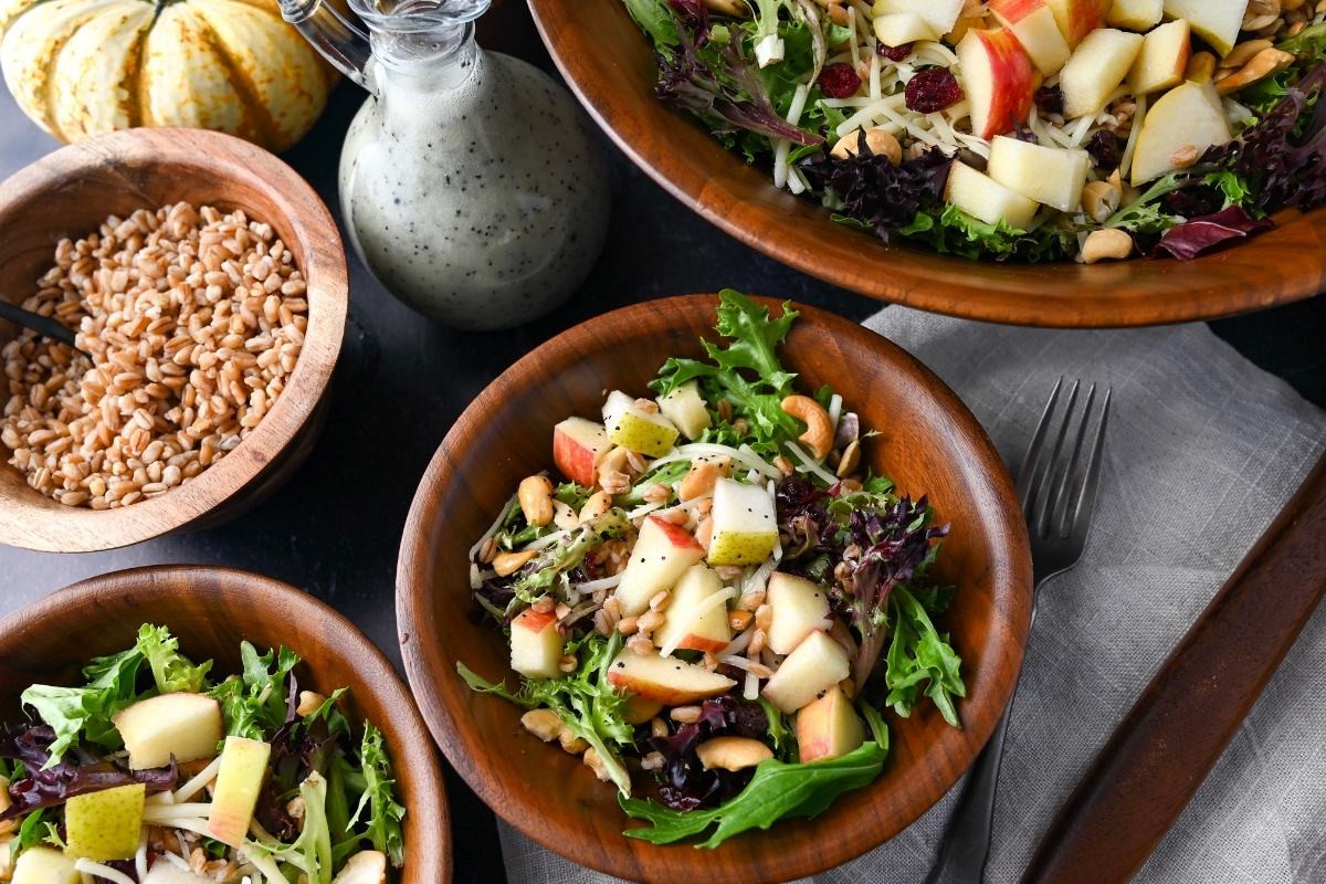 farro salad in bowls with a bowl of cooked farro and a container of salad dressing