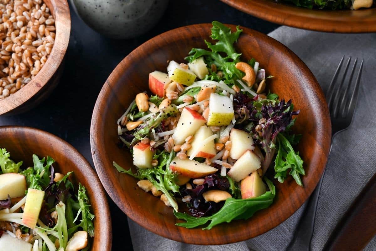 two farro salads in wood bowls next to a bowl of cooked farro