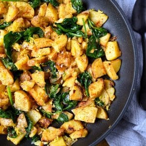 photo of caramelized gold potatoes, and spinach in a gray skillet