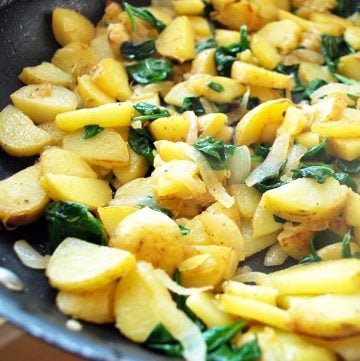 sauteed potatoes with wilted spinach and onions in a skillet
