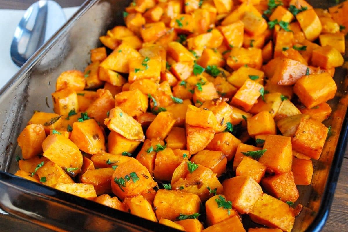 side view of a pan of cooked roasted sweet potatoes tossed in olive oil, garlic, rosemary, and fresh parsley