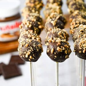 close up of nutella cake pops covered in chopped hazelnuts with a jar of nutella in the background