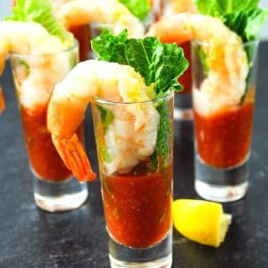 four mini parfait glasses with shrimp, cocktail sauce, lemon zest, and a romaine leaf