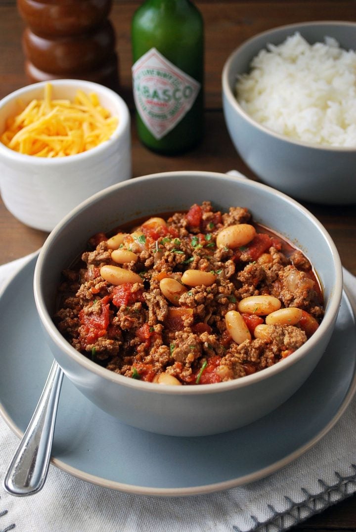 overhead shot of bowl of chili with topping ingredients in background