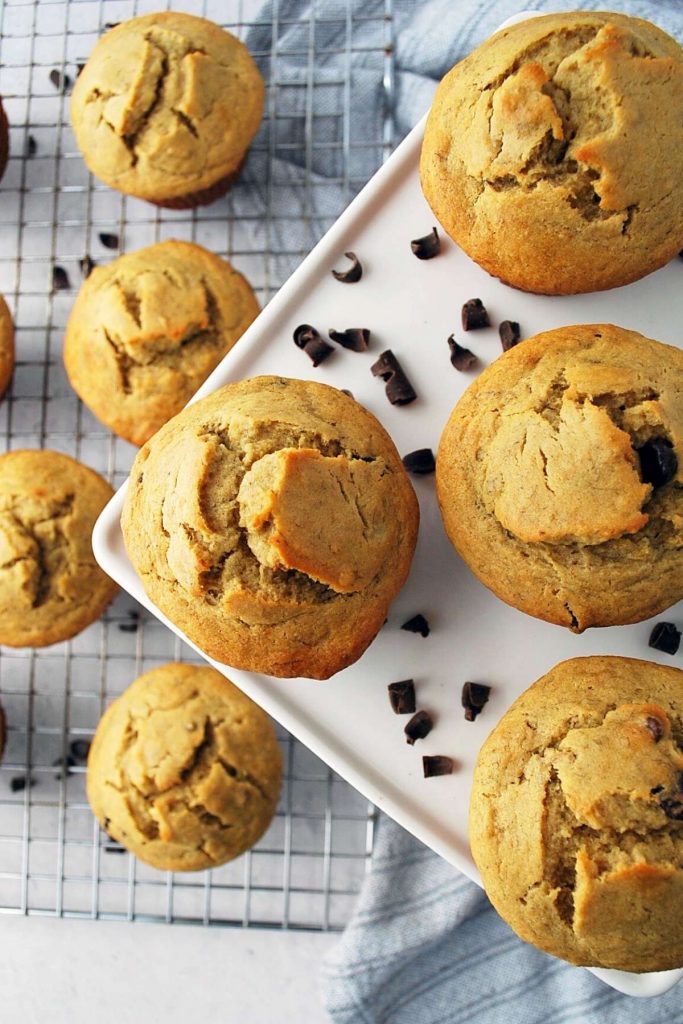 gluten-free banana chocolate chip muffins on a platter with a baking rack of muffins underneath