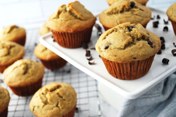 gluten free banana chocolate chip muffins on a cooling rack and a few muffins on a platter on the side