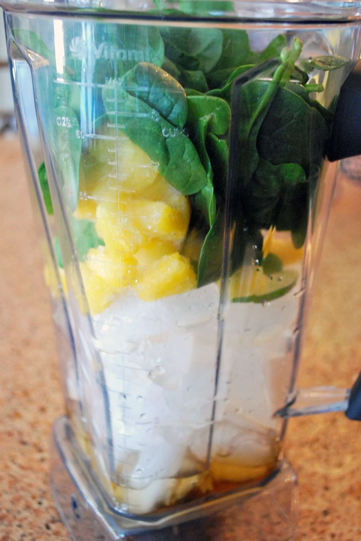 mango, spinach, and ice in a blender canister