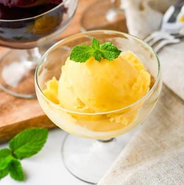 a clear parfait dish with a scoop of mango pineapple sorbet with a mint sprig on top