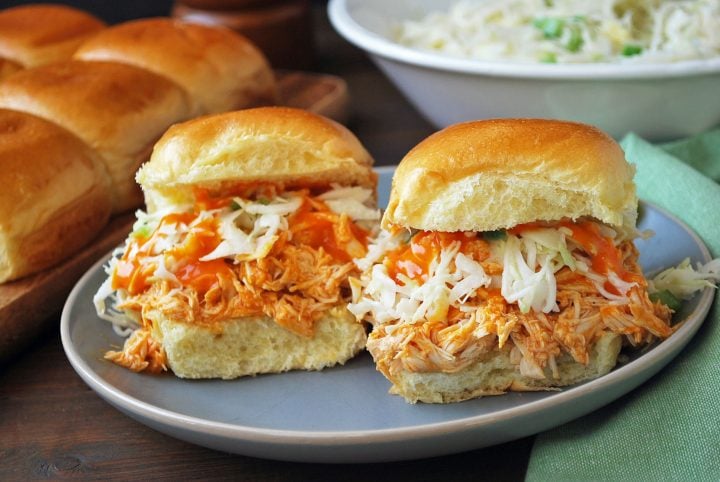 buffalo sliders plated with slaw and hot sauce with rolls in background