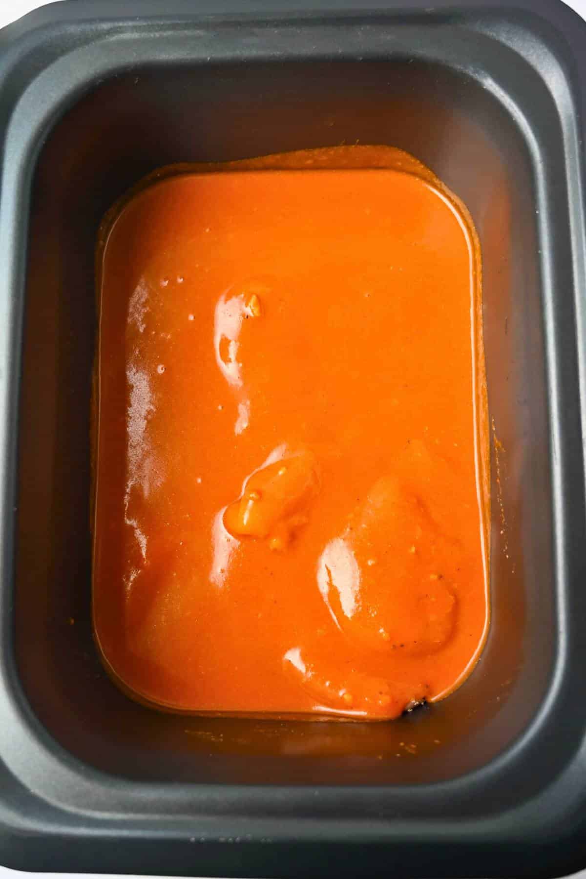 chicken breasts with a buffalo sauce on top in a slow cooker