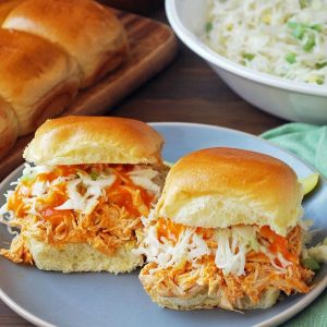 two buffalo sliders on a plate with slaw and rolls in background