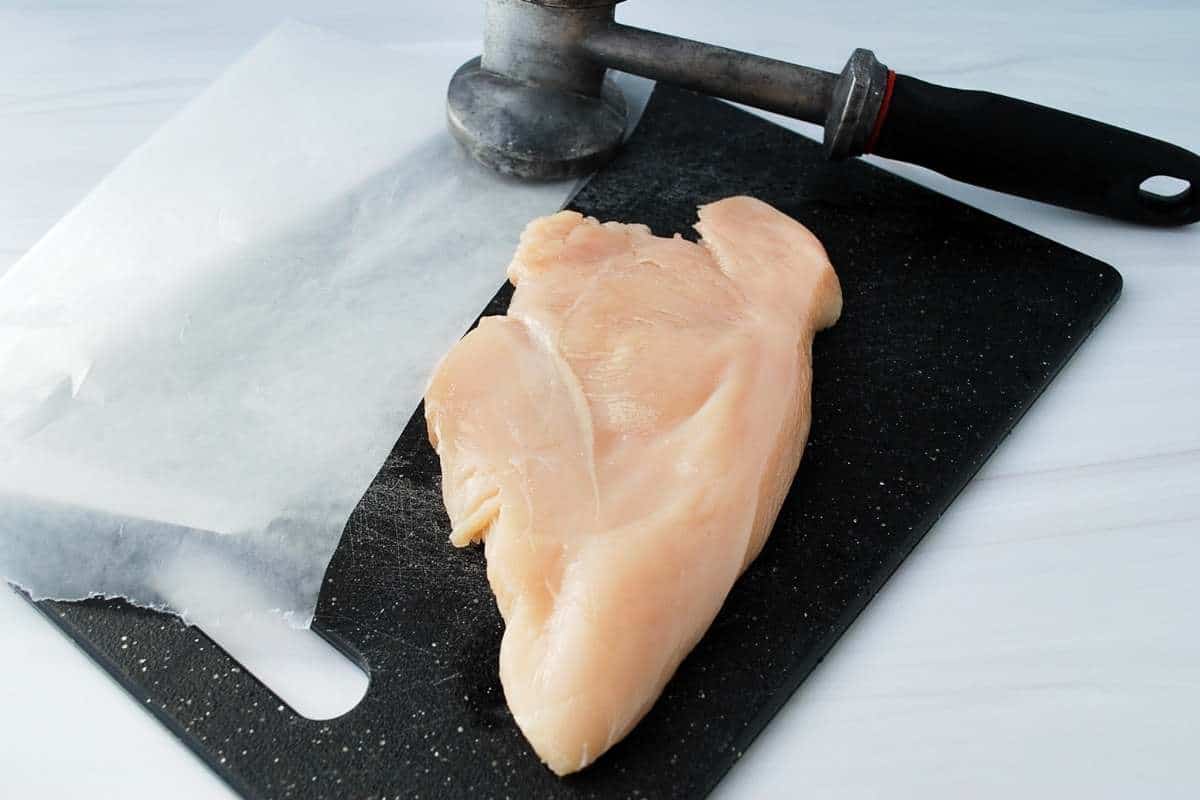 chicken breast and meat mallet on a cutting board with wax paper