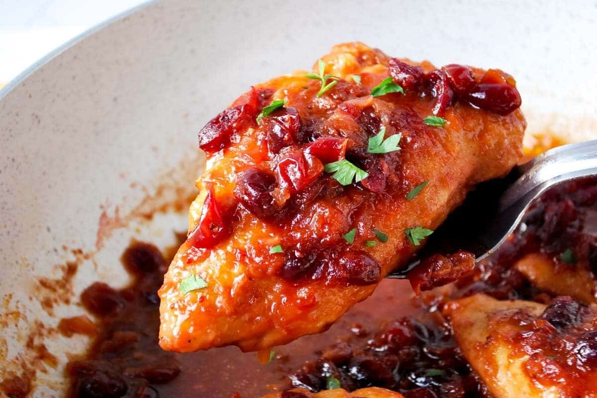 a chicken breast covered in orange cranberry sauce lifted up with a spoon