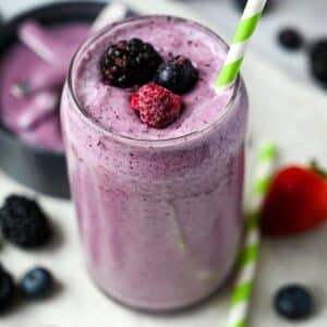 a mixed berry shake with frozen berries on top with a straw