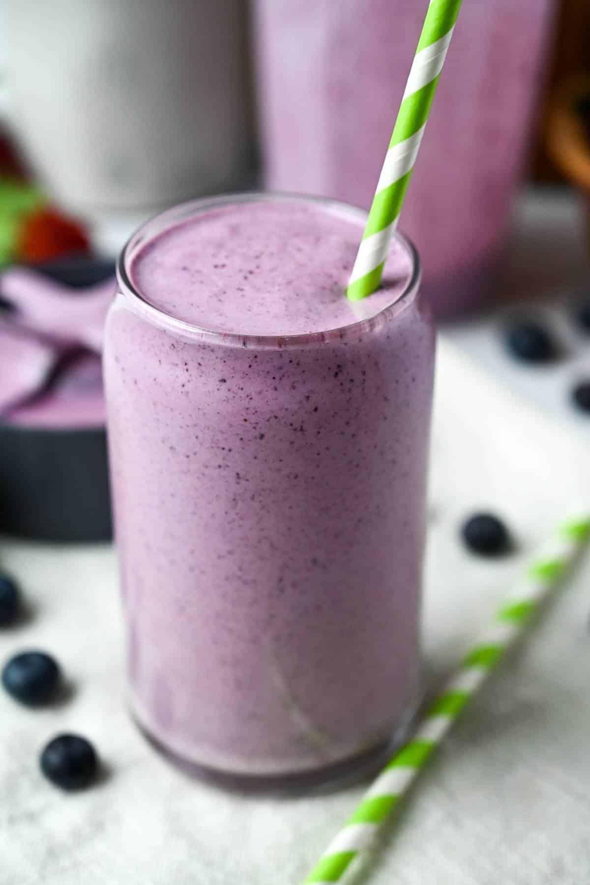 a berry smoothie in a glass with a green striped straw