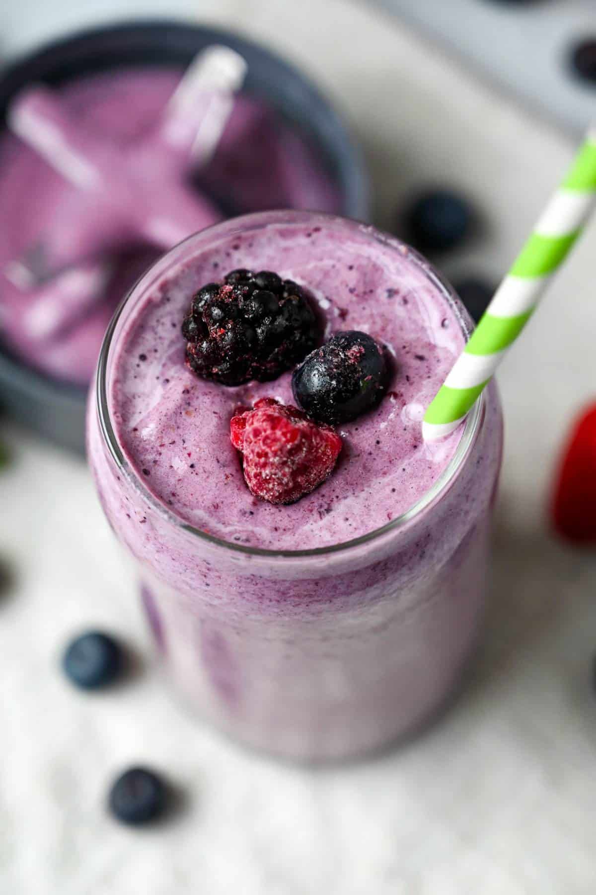 looking down into a smoothie in a glass with a frozen blackberry, raspberry and blueberry on top with a straw