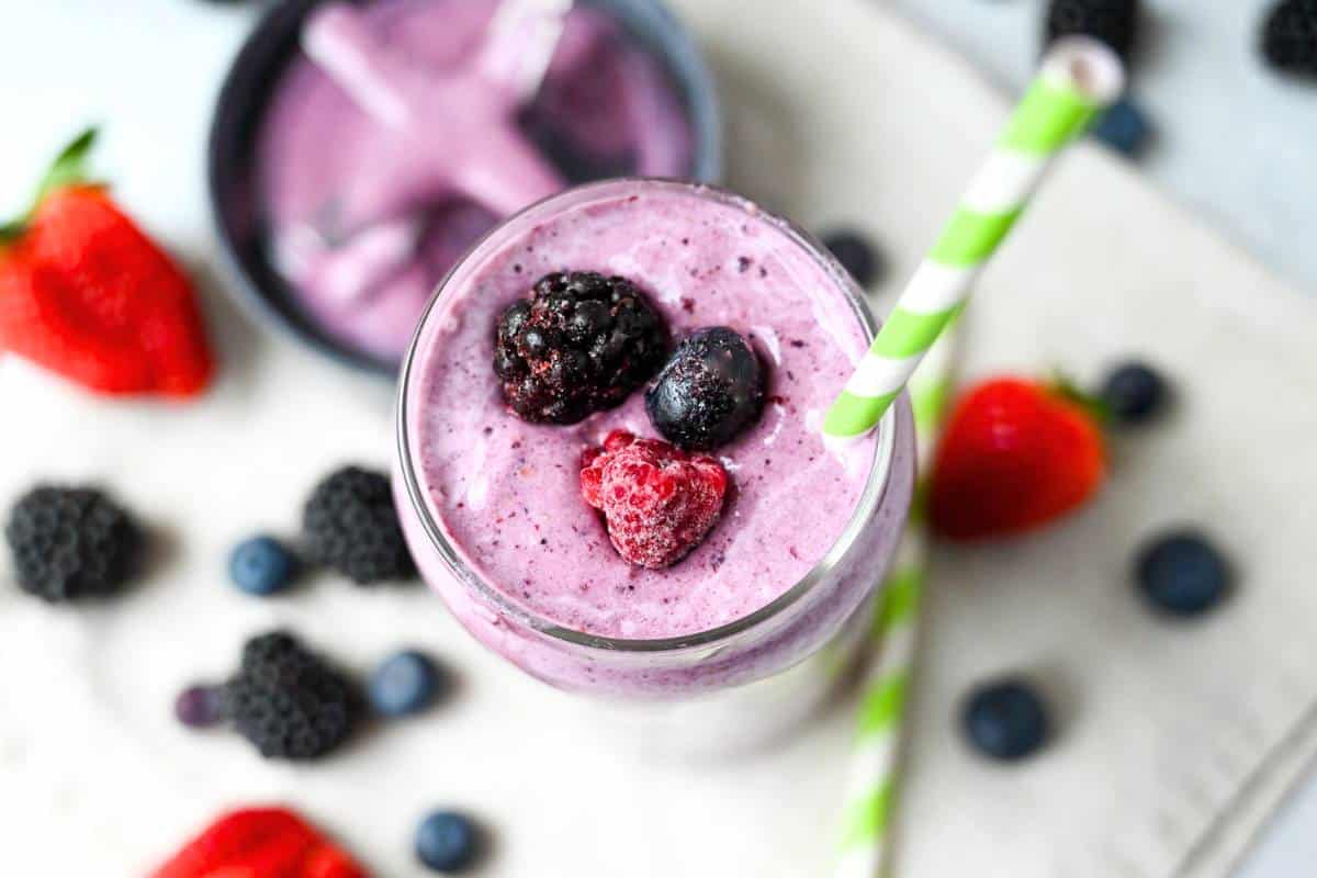 the top of a protein shake with frozen fruit with mixed berries on the table around it and the top of a blender jar