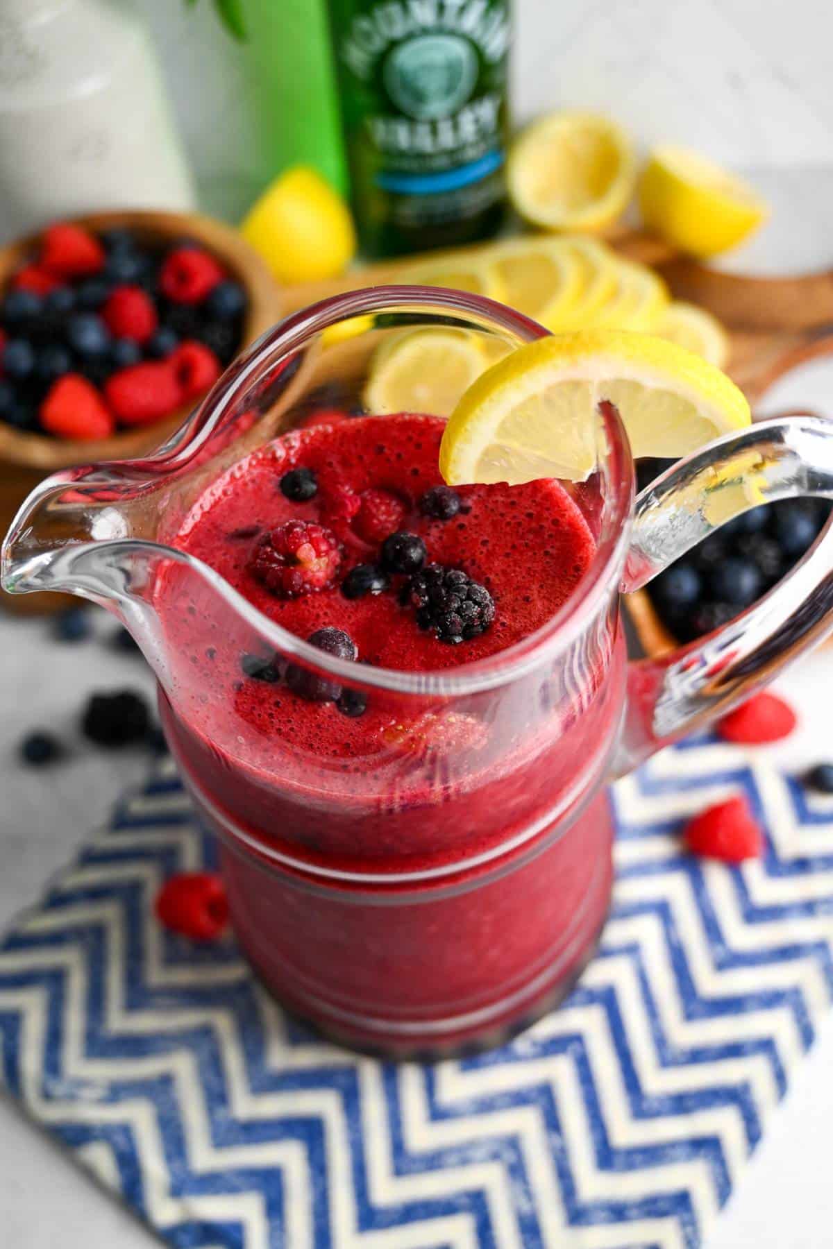 a pitcher of berry lemonade with frozen berries on top