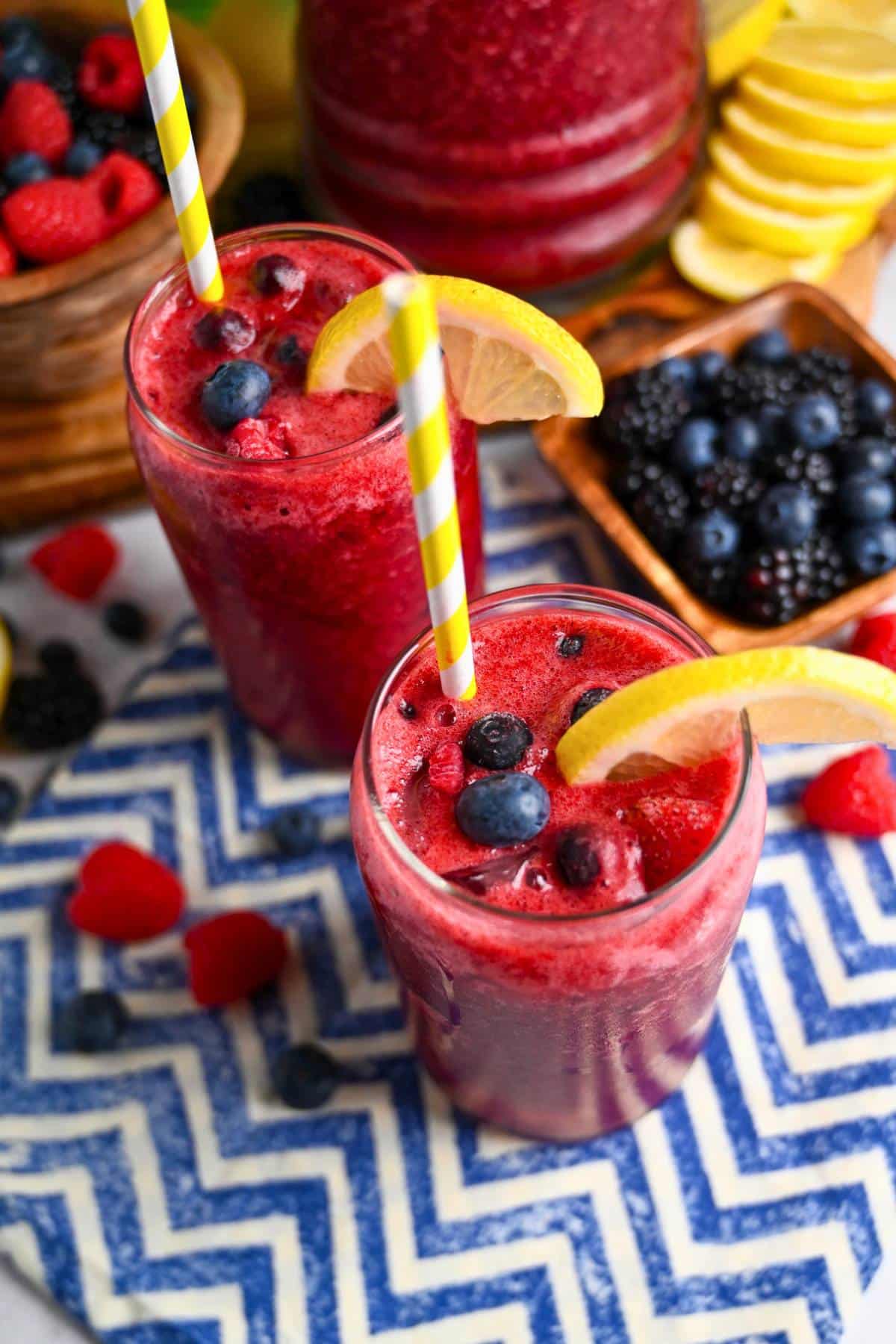 two glasses of sparkling mixed berry lemonade with lemon slices on the rim and a yellow striped straw