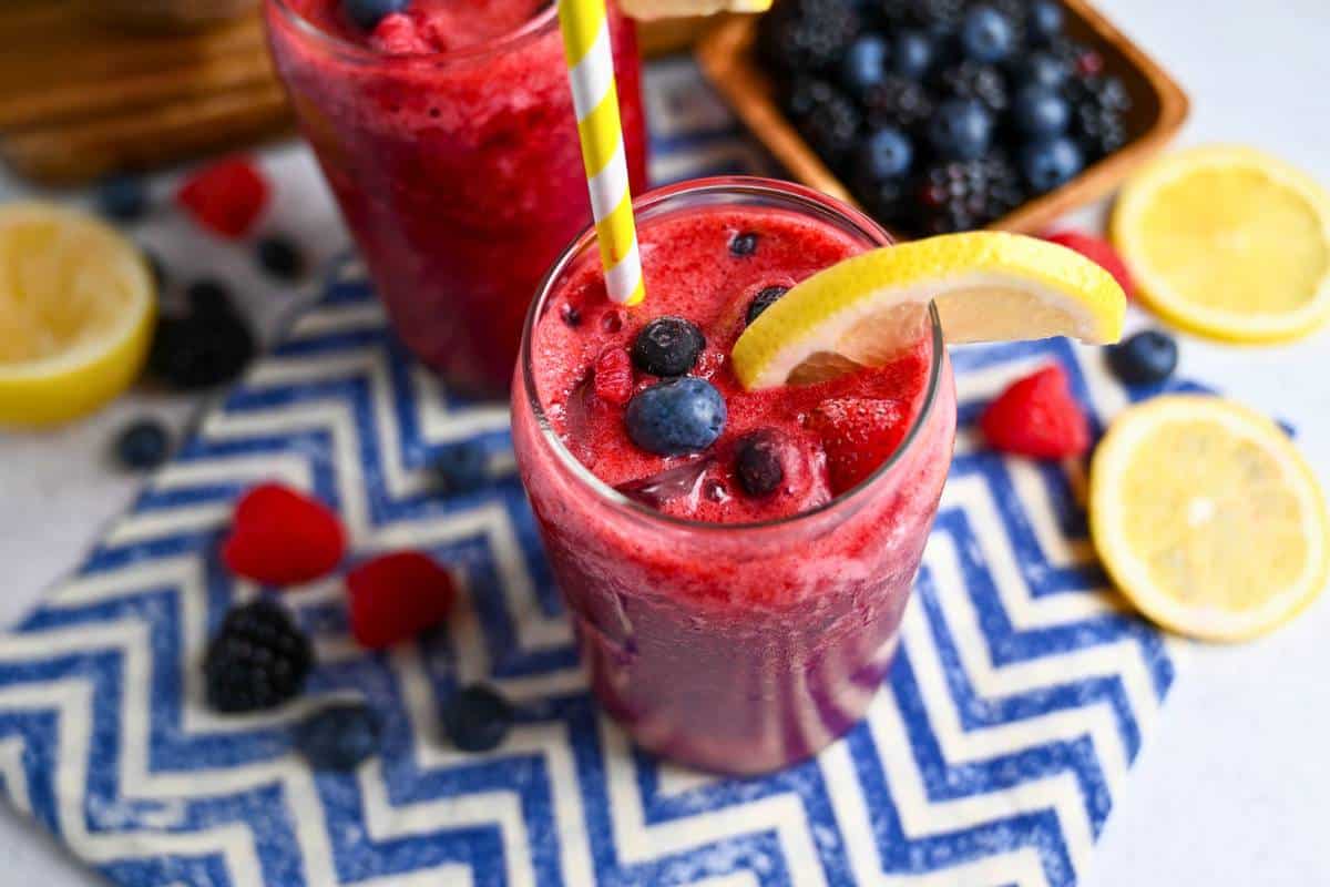 side view of a sparkling berry lemonade mocktail with lemon slices and berries around it