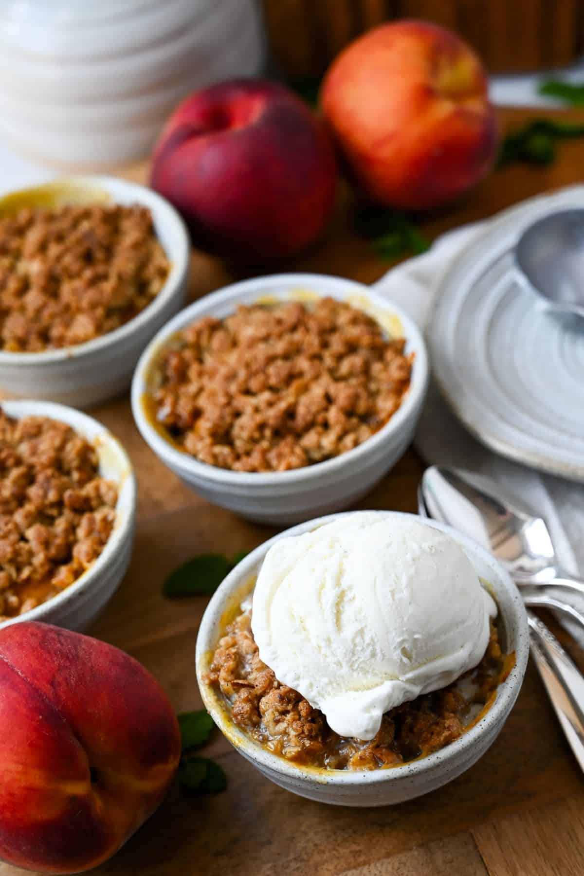 a peach next to a dish of peach crumble topped with a scoop of ice cream 