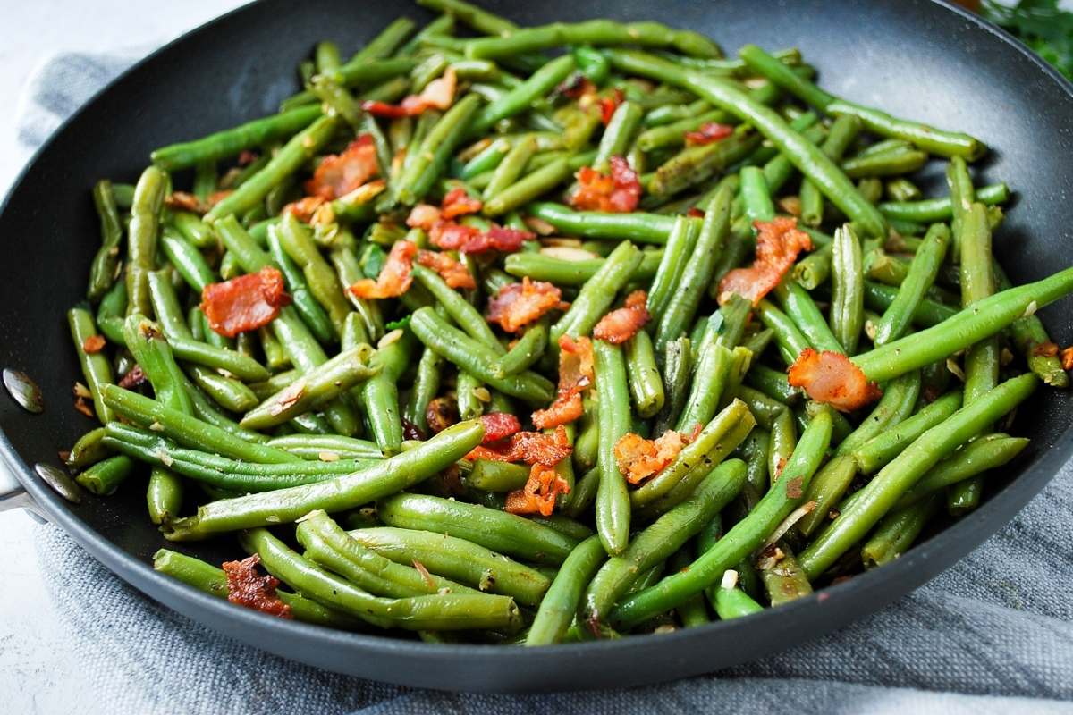 side view of a skillet of green beans almondine with bacon