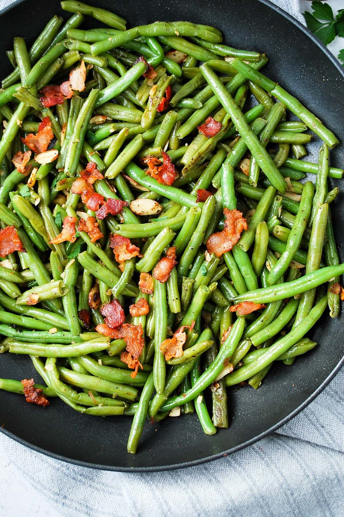 overhead photo of green beans almondine in a skillet topped with crumbled bacon