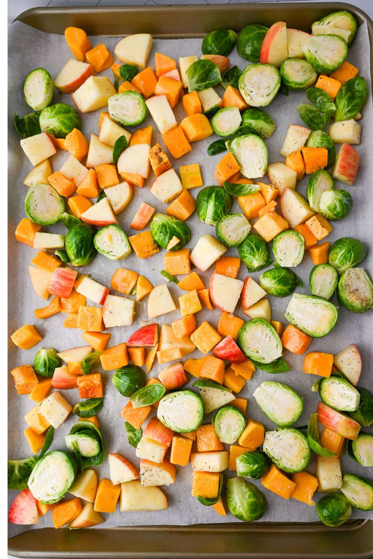 apples, brussels sprouts, and butternut squash spread out on a parchment lined baking sheet