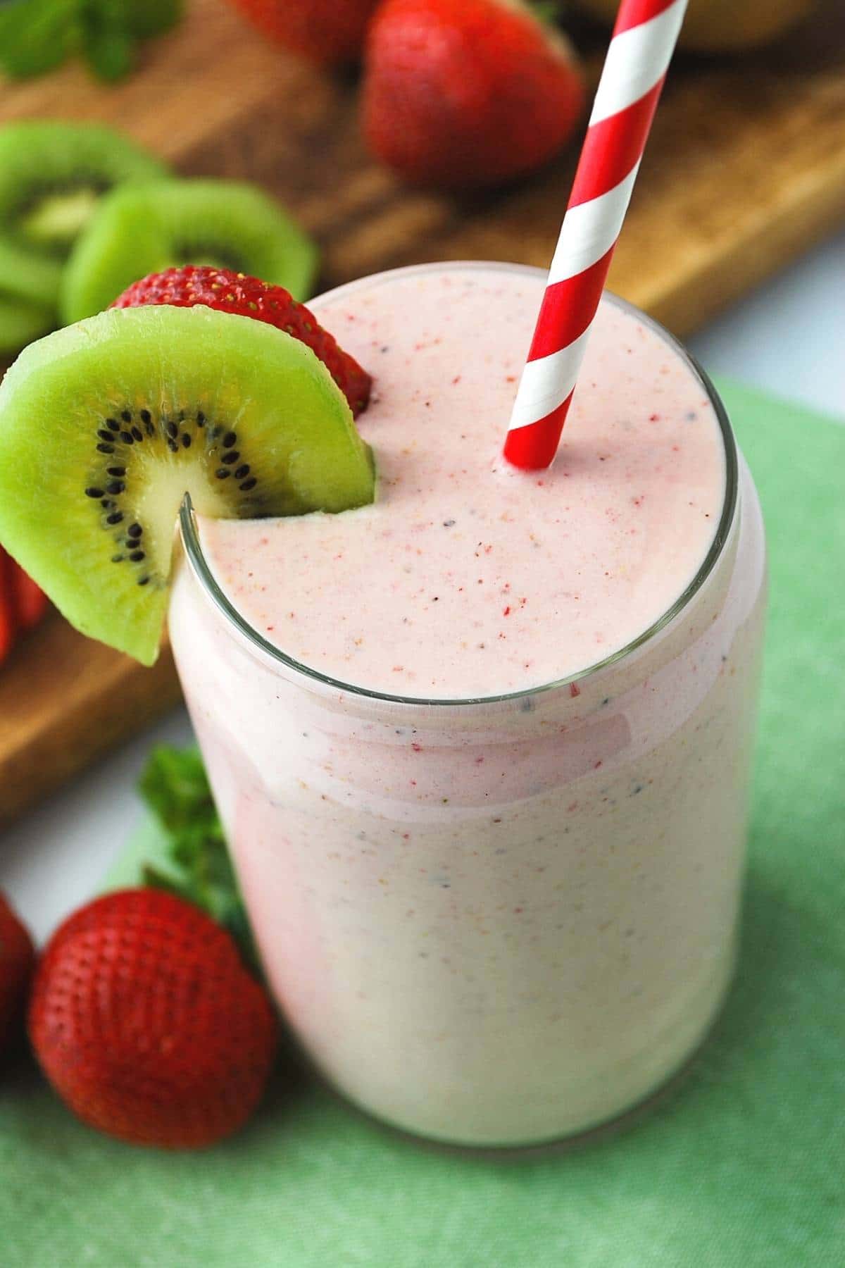 overhead photo of a strawberry kiwi banana smoothie with a red striped straw and a slice of kiwi and strawberry on the rim