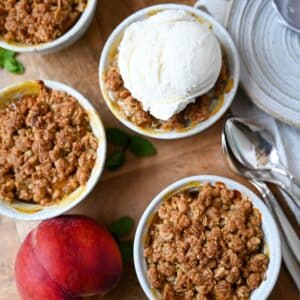 peach crisp in ramekins with a peach next to it and a scoop of vanilla ice cream