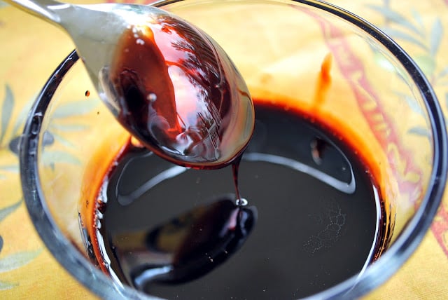 A close up of balsamic reduction in a glass dish coating the back of a spoon