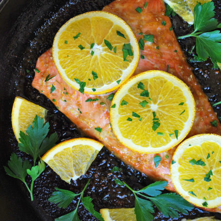 Baked salmon topped with orange slices and herbs in a cast iron skillet