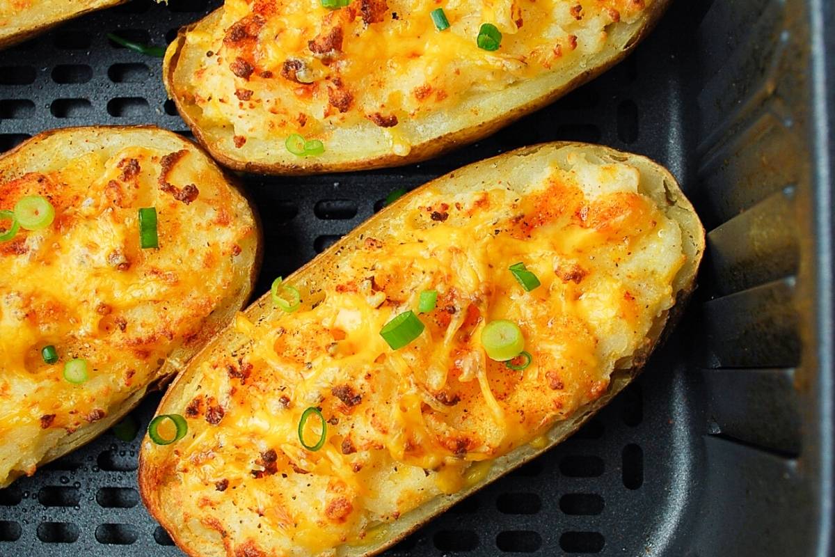 close up of three twice baked potatoes in an air fryer basket garnished with chives