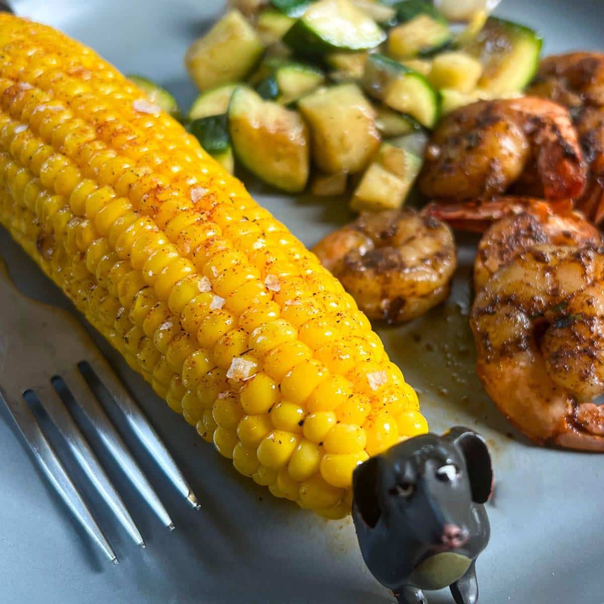 corn on the cob on a plate with shrimp and zucchini