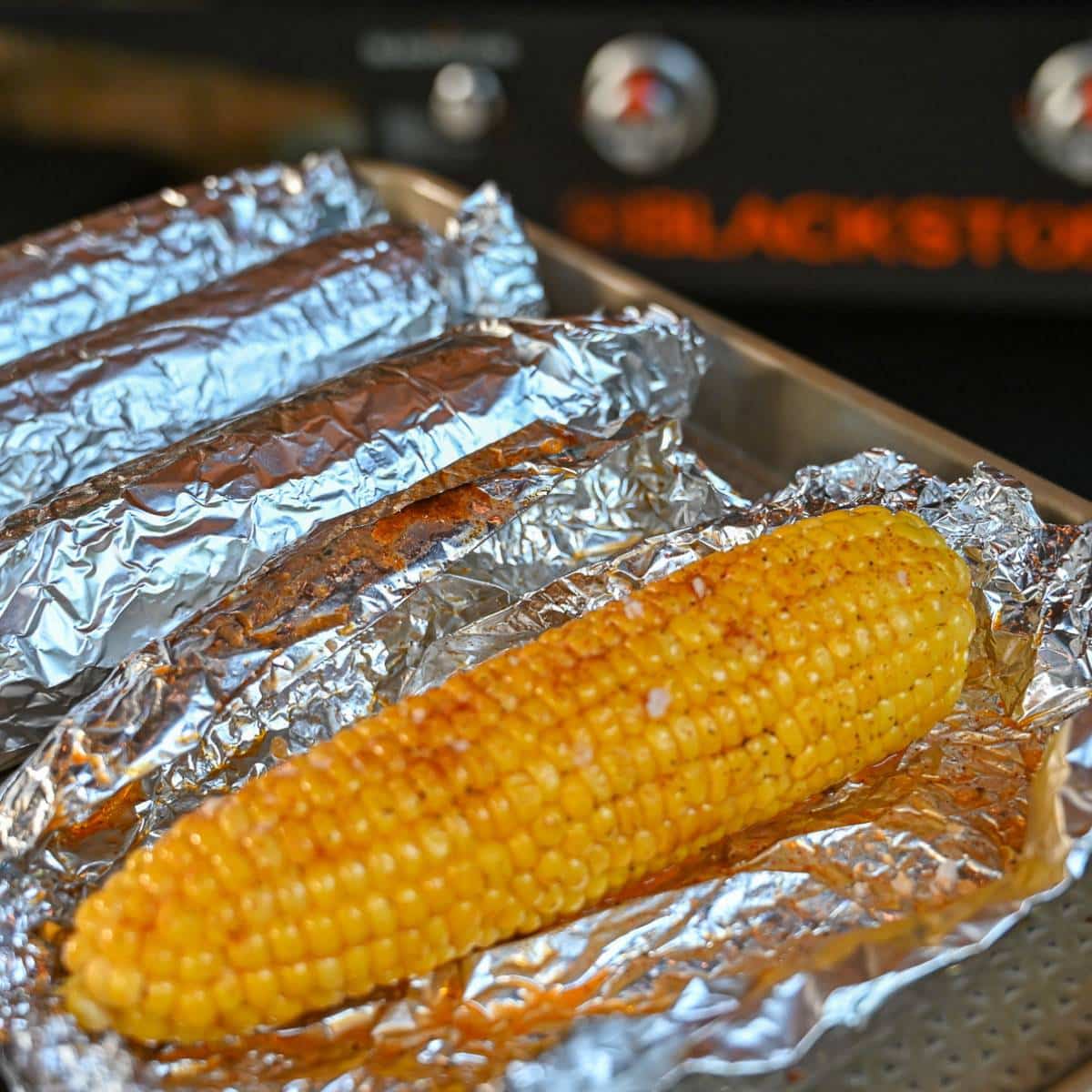 a seasoned and cooked ear of corn in foil with a blackstone griddle in the background
