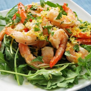 close up photo of marinated shrimp on a bed of greens with fresh herbs on top