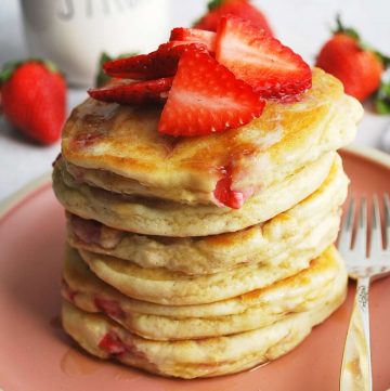 close up of a stack of gluten free protein pancakes with fresh strawberries and a fork on the side