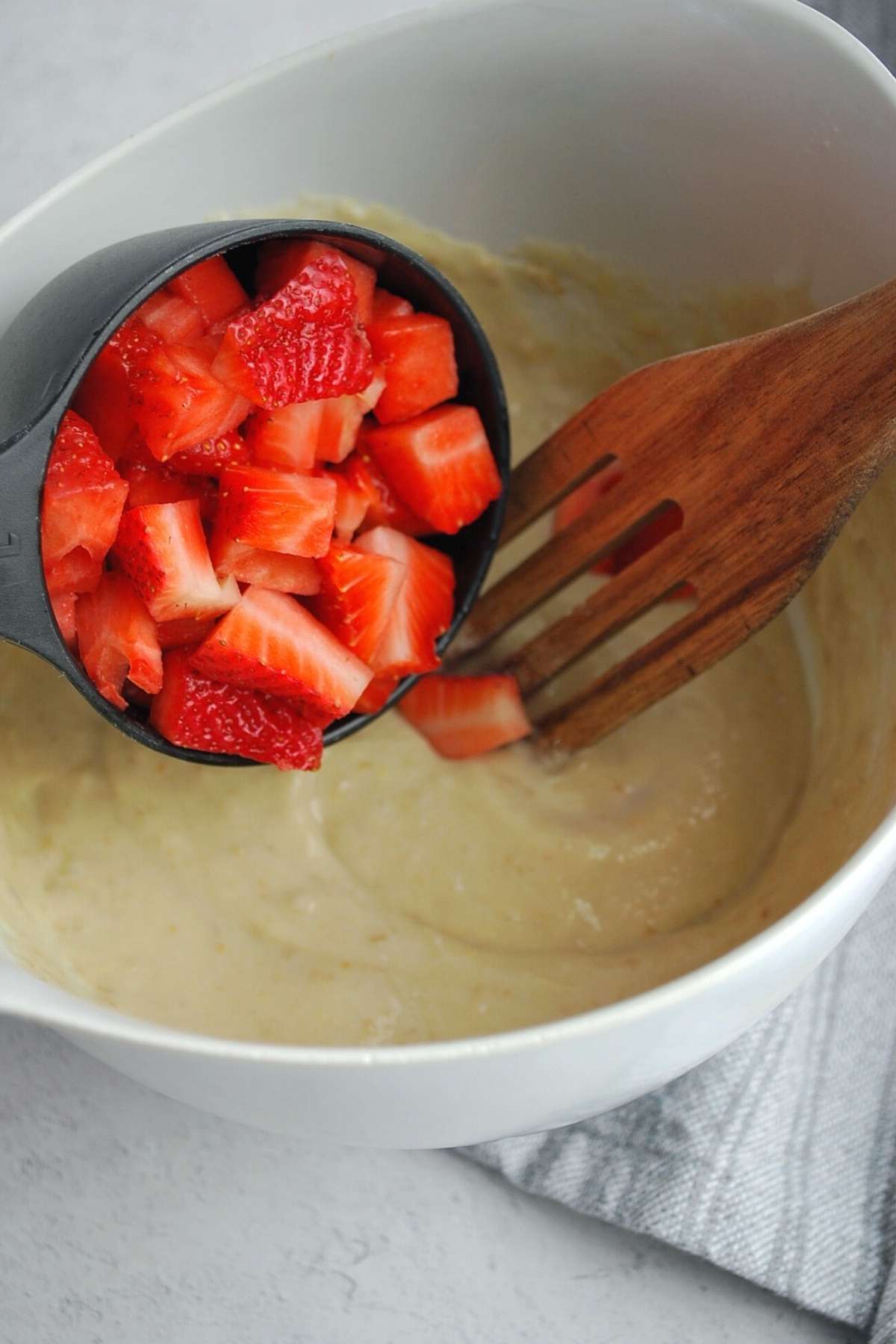 Adding fresh strawberries to pancake batter in a bowl