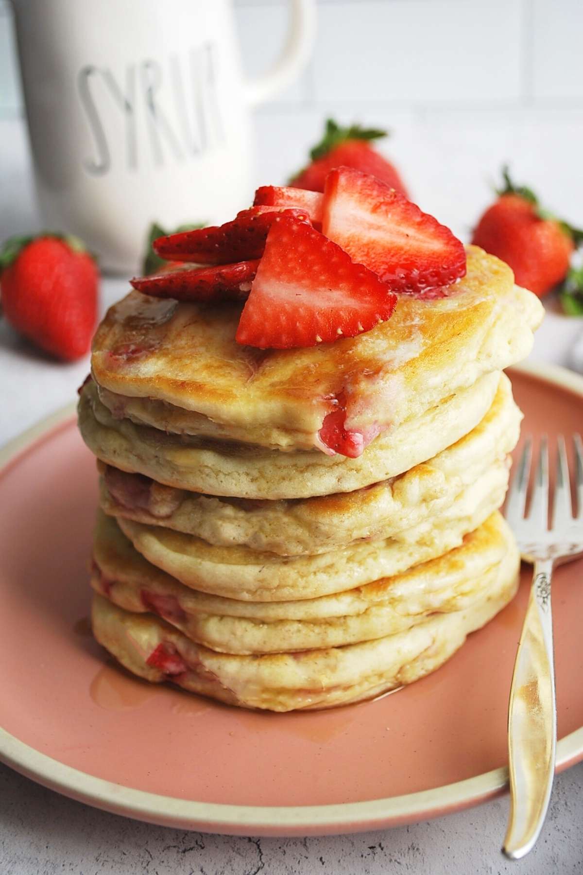 A tall stack of fresh strawberry pancakes topped with strawberries