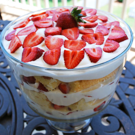 A strawberry trifle topped with fresh strawberries on a table outdoors