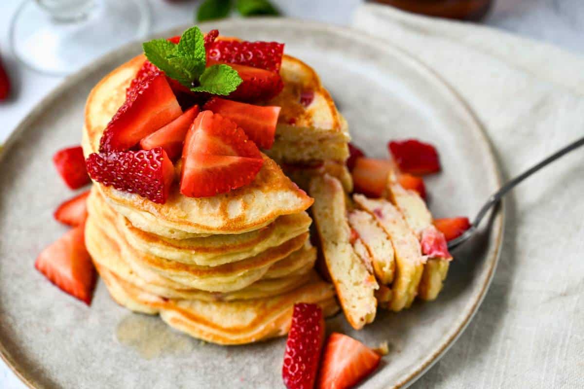 a bite cut out of a stack of pancakes with strawberries