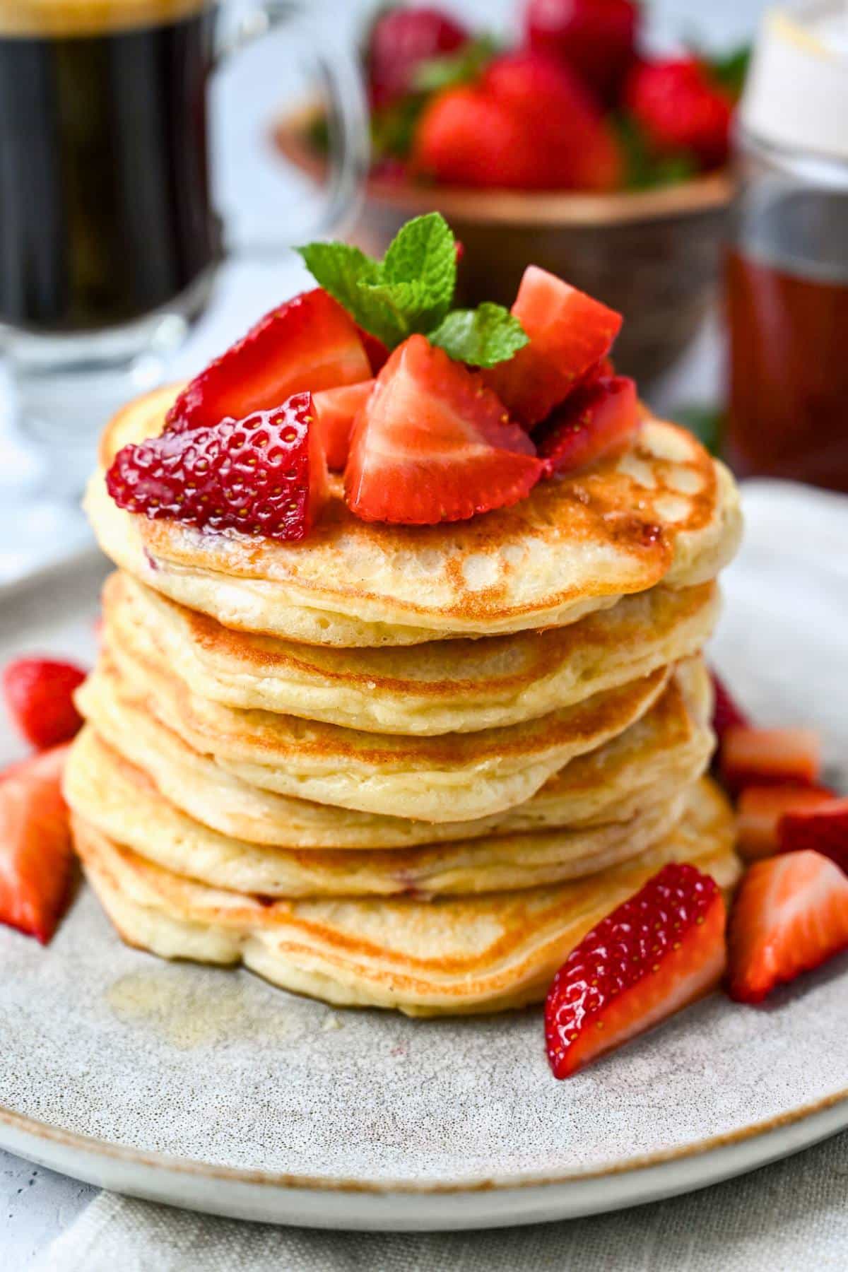 a tall stack of strawberry pancakes with fresh strawberries and a sprig of mint on top