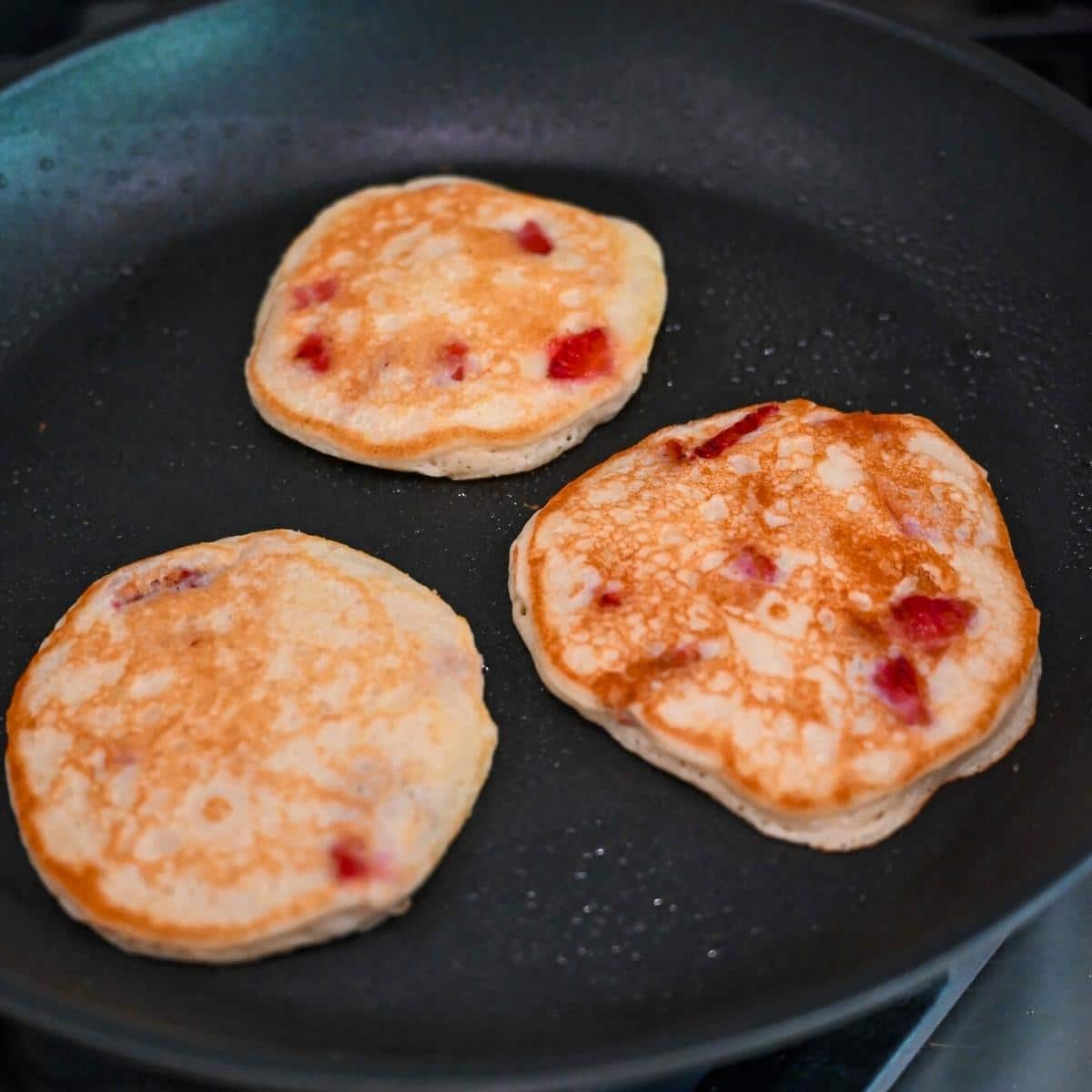 strawberry pancakes cooking in a skillet