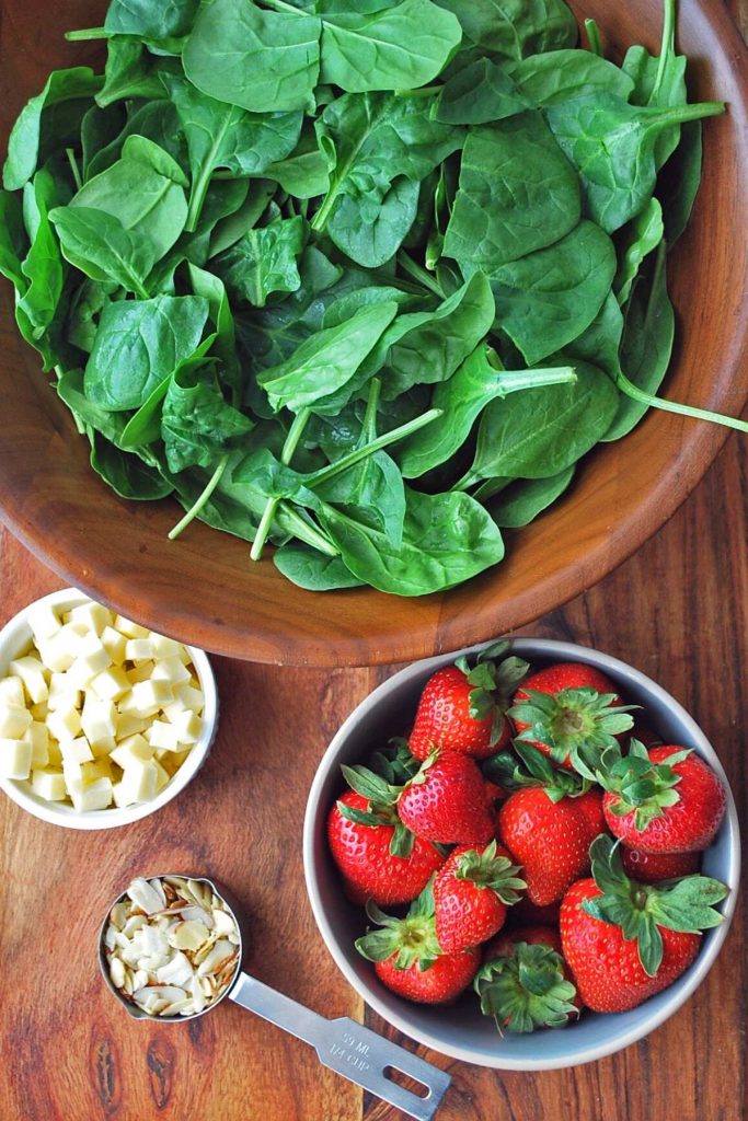 ingredients for strawberry spinach salad on a wood cutting board
